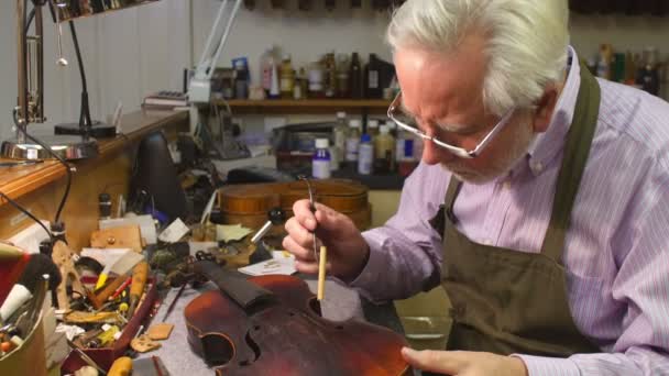 Человек восстанавливает скрипку в мастерской — стоковое видео