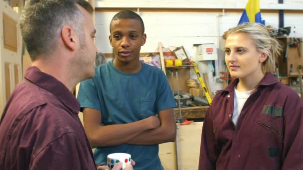 Плотник беседует с учениками в занятой мастерской — стоковое видео