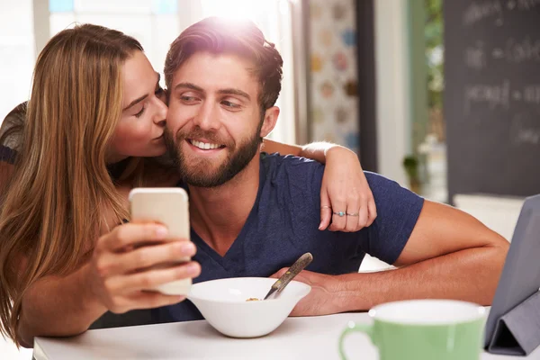 Casal comendo café da manhã usando tablet digital e telefone — Fotografia de Stock