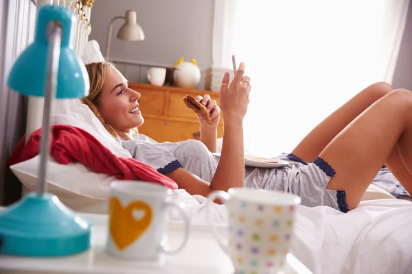 Kvinna liggande på sängen med mobiltelefon — Stockfoto