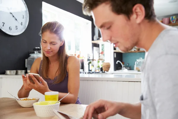 デジタル タブレットと電話を使用した朝食を食べるカップル — ストック写真