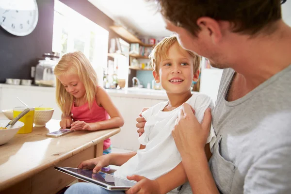 Padre e hijos usando dispositivos digitales en la mesa de desayuno — Foto de Stock