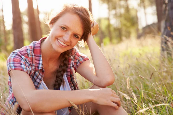 Sorridente giovane donna seduta in campagna — Foto Stock