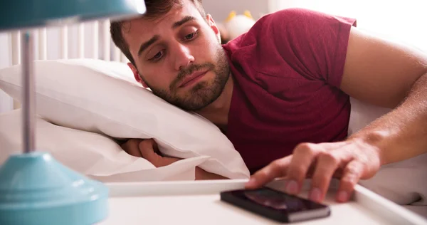 Uomo a letto svegliato da allarme sul telefono cellulare — Foto Stock