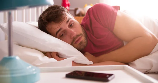 Homme au lit réveillé par alarme sur téléphone portable — Photo