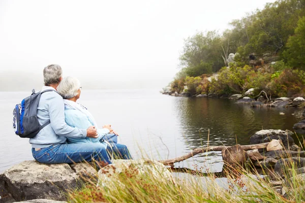 Старшая пара, сидящая вместе у озера — стоковое фото