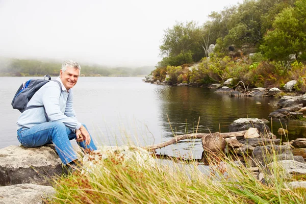 Усміхнений старший чоловік сидить біля озера — стокове фото