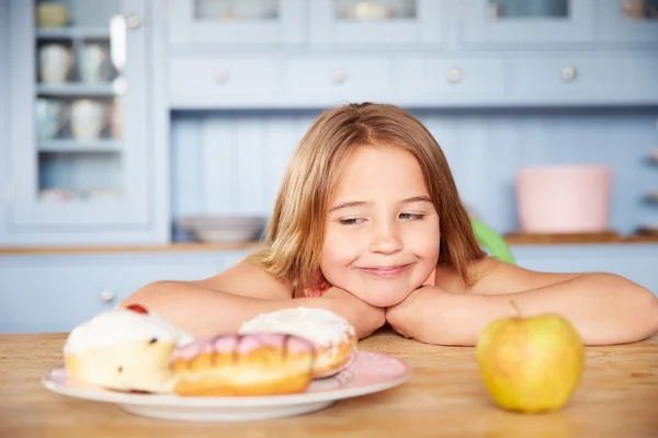 Menina escolhendo bolos ou maçã para lanche — Fotografia de Stock