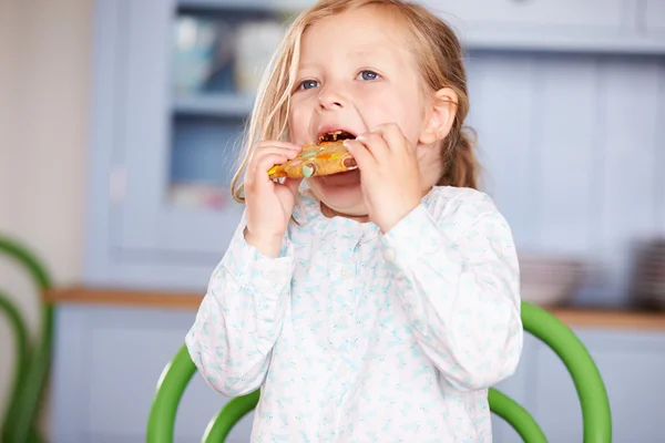 Menina jovem sentada na mesa comer biscoito — Fotografia de Stock