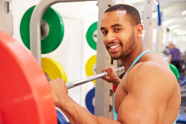 Mann mit Langhanteln auf einem Gepäckträger in einem Fitnessstudio — Stockfoto