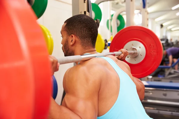 Człowiek w podnoszeniu ciężarów sztanga w squat rack — Zdjęcie stockowe