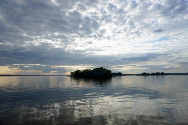       Sıcak bir yaz gününde gölün üzerinde gün batımı. Haziran gökyüzü ve güzel bulutlar. Ufuk ve yansıma. Suyun pürüzsüz yüzeyi.                          