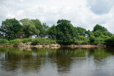       Yaz sıcağı. Temmuzda Pripyat nehri. Bulutlar ve gökyüzü. Kıyıdaki meşeler ve ağaçlar. Yansıma                         