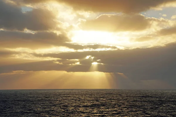 Bright colorful sunrise in the open ocean. Atlantic. The sun\'s rays make their way through the clouds.