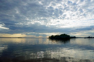    Sıcak bir yaz gününde gölün üzerinde gün batımı. Haziran gökyüzü ve güzel bulutlar. Ufuk ve yansıma. Suyun pürüzsüz yüzeyi.                            