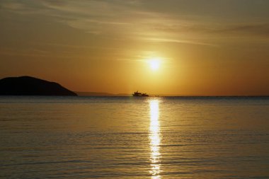     Ege Denizi üzerinde parlak kırmızı gün batımı. Güneş ve dağlar. Geminin silueti ve silueti. Dalgalar ve parıltılar.                           