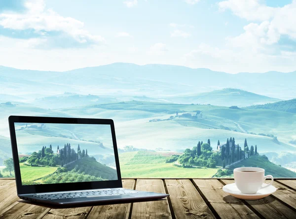 Ноутбук и чашка кофе на столе, Тоскана, Италия в качестве фона — стоковое фото