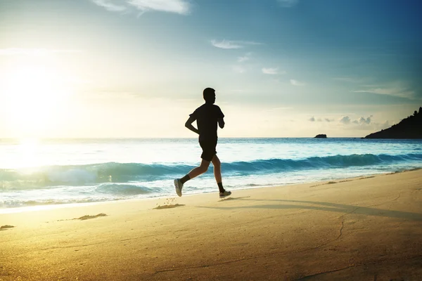Mężczyzna biegający po tropikalnej plaży o zachodzie słońca — Zdjęcie stockowe