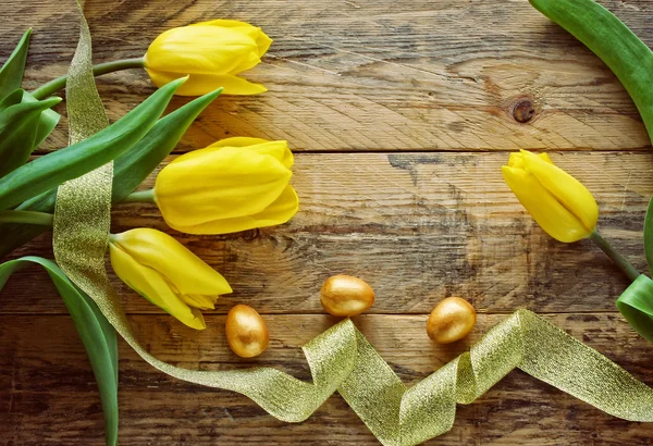 Tło Wielkanoc z żółtych tulipanów, złote jaja — Zdjęcie stockowe