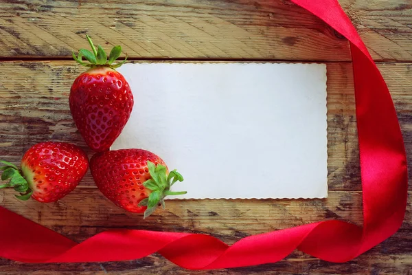 Erdbeeren, rotes Satinband und leeres Papieretikett — Stockfoto