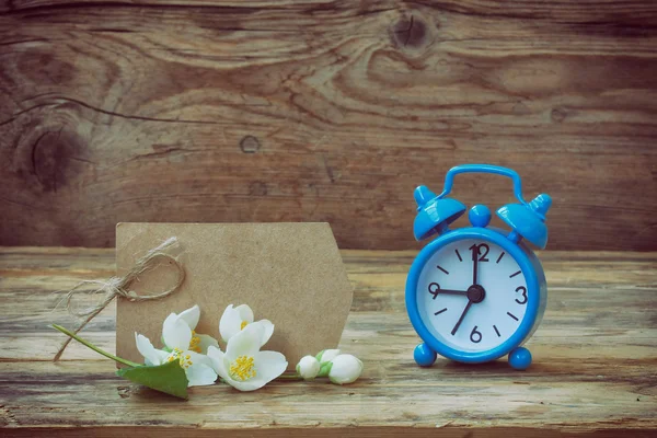 Blue alarm clock, empty paper tag, jasmine branch — Stock Photo, Image