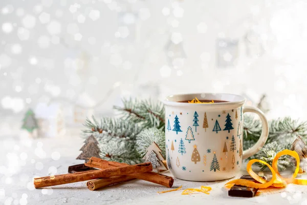 Cozy winter composition with a cup of hot chocolate and snow-covered branches on a bright festive background. Christmas or winter drink concept.