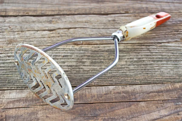 Old rusty potato masher on wooden background — Stock Photo, Image