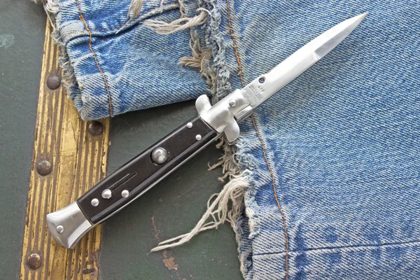 Switchblade knife on old blue jeans — Stock Photo, Image