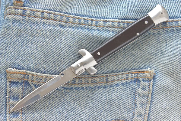 Switchblade knife on old blue jeans — Stock Photo, Image