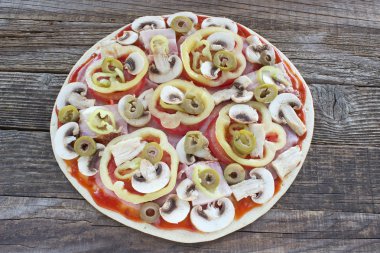 Ahşap masa üzerinde malzemelerle çiğ pizza