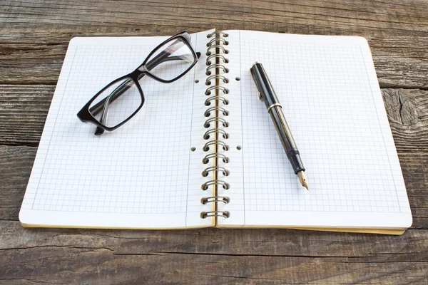 Fountain pen and spiral notebook with eyeglasses on wooden table — Stock Photo, Image