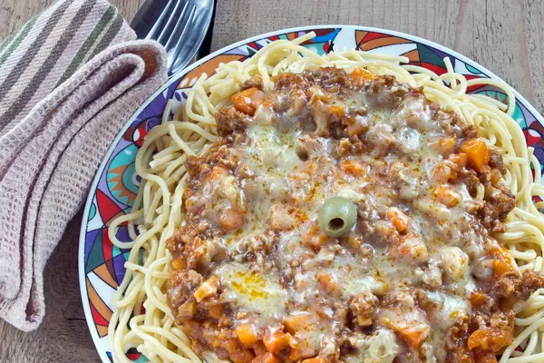 Спагетти болоньезе на тарелке с вилкой и ложкой на столе — стоковое фото