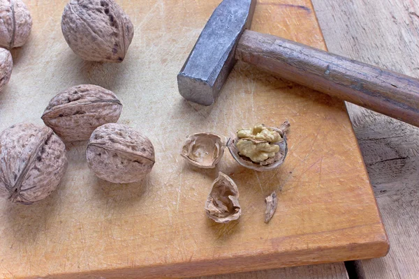Gebarsten walnoten en hammer op oude houten bord — Stockfoto