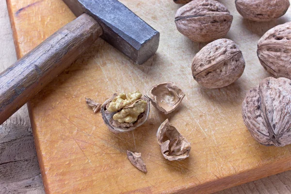 Cracked walnuts and hammer on old wooden board — Stock Photo, Image