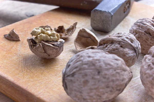 Cracked walnuts and hammer on old wooden board — Stock Photo, Image