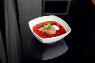 Siyah zemin üzerinde beyaz bir tabakta yansıması olan et çorbası.