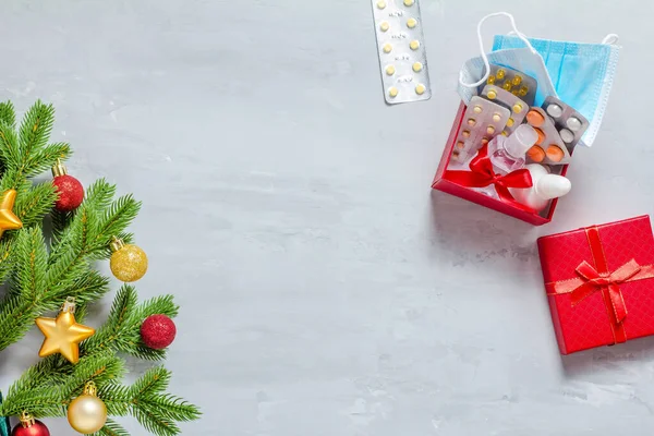 Ramo di abete rosso decorato con giocattoli di Natale, regali con farmaci, pillole, maschera medica e antisettico su uno sfondo concreto. Copia spazio, vista dall'alto — Foto Stock