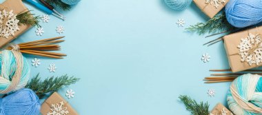 Örgü aletleriyle Noel kompozisyonu. Noel hediyeleri, köknar dalları, iplik, örgü iğneleri ve mavi arka planda örülmüş kar taneleri. Düz konum, üst görünüm, kopyalama alanı. Yeni Yıl