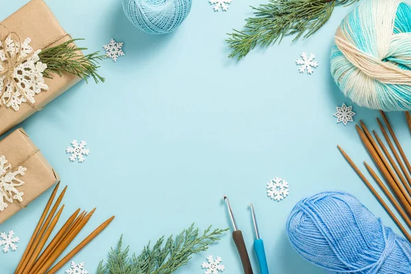 編物ツールとクリスマスの組成。青い背景にクリスマスプレゼント、モミの枝、糸、編み針や編んだ雪片。フラットレイアウト、トップビュー、コピースペース。新年 ストック画像