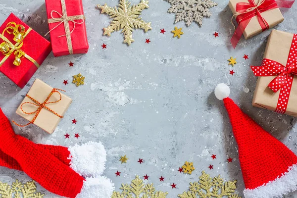 Cappello e sciarpa di Babbo Natale, scatole regalo, fiocchi di neve dorati e stelle rosse su sfondo grigio cemento, sotto forma di cornice. La vista dall'alto. Buon Natale, Anno nuovo — Foto Stock