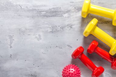 Fitness geçmişi. Spor salonu ve ev aletleri. Kırmızı ve sarı halterler ve beton arka planda bir masaj topu. Üst görünüm, kopyalama alanı