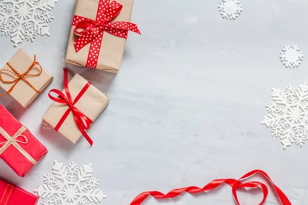 Scatole regalo avvolte in carta artigianale e rossa, nastri rossi e fiocchi di neve bianchi su sfondo grigio cemento, sotto forma di cornice. La vista dall'alto. Buon Natale, Anno nuovo — Foto Stock