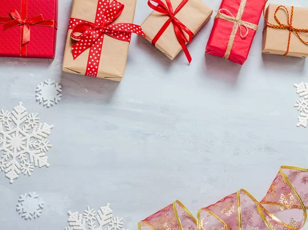 Cajas de regalo envueltas en papel artesanal y rojo, cintas rojas y copos de nieve blancos sobre un fondo de hormigón gris, en forma de marco. La vista desde arriba. Feliz Navidad, Año Nuevo — Foto de Stock