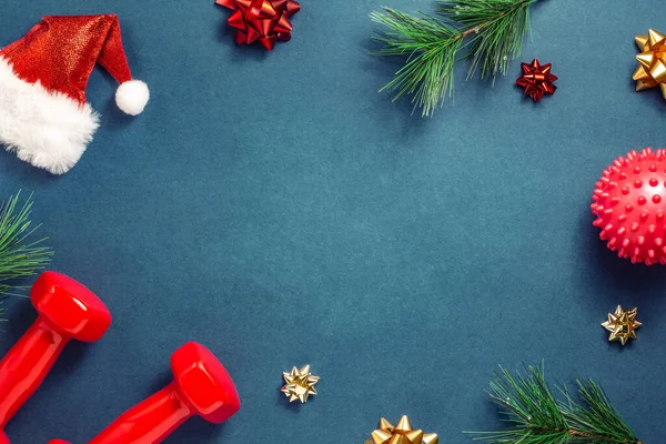 Fitness koncept Veselé Vánoce a šťastný Nový rok. Červené činky, luky, Santa klobouk, masážní míč a vánoční stromeček na modrozeleném pozadí. Horní pohled, kopírovací prostor — Stock fotografie