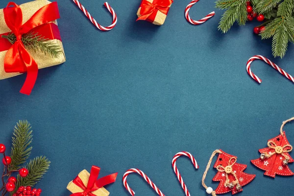 Composizione natalizia. Alberi di Natale rossi di legno, un ramo di abete con bacche, regali con nastri rossi, lecca-lecca su uno sfondo blu scuro. Capodanno. Layout piatto, vista dall'alto, spazio di copia — Foto Stock