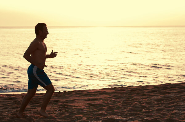 Красивый мужчина бежит по пляжу на закате

