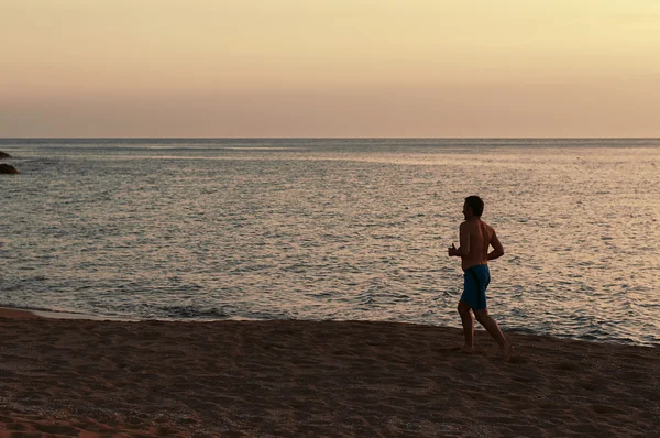 Bonito homem em forma correndo na praia do pôr do sol — Fotografia de Stock