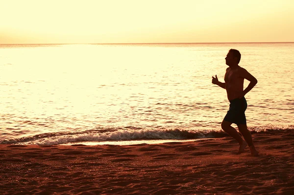 Bonito homem correndo na praia do pôr do sol — Fotografia de Stock