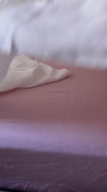 Dikey 4K 'lık kadın eli, tozlu pembe keten çarşaflarla yatağı toplarken. Konforlu ev içi ve ev idaresi kavramı.