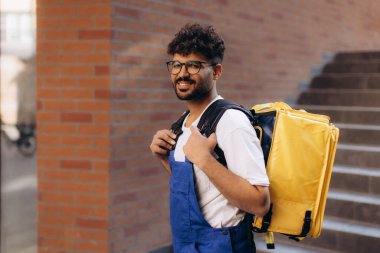 Sarı termal sırt çantası taşıyan mavi üniformalı bir kurye. Şehir caddesinde yiyecek dağıtıyor.